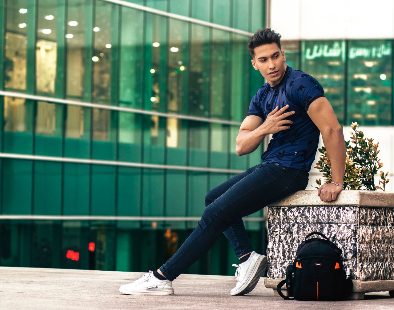 Man posing confidently by a modern glass building in Tabriz, Iran.
