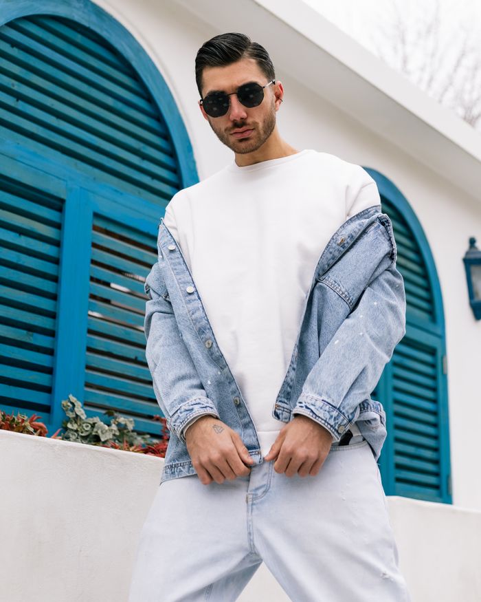 about-img Stylish man in jean jacket and sunglasses posing against blue shutters outdoors.