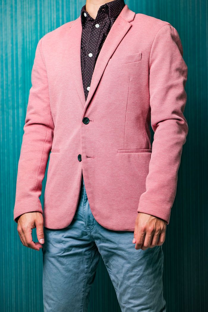 A man showcases a fashionable pink blazer paired with casual jeans in a studio setting.
