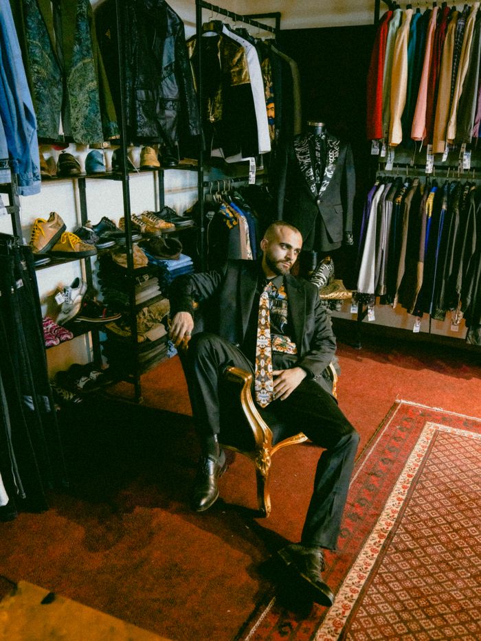 Man in a vintage clothing store surrounded by colorful outfits and trendy accessories.